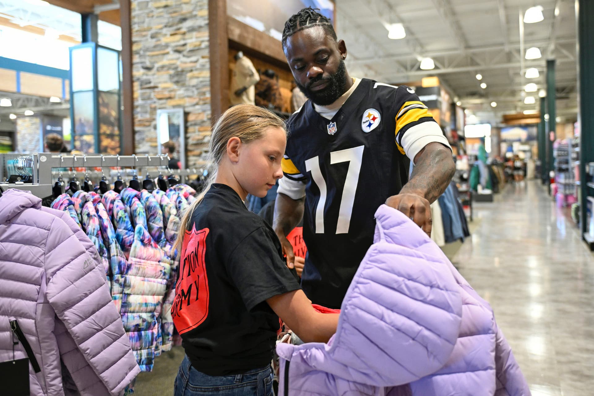 Ayo Oyelola helping a young girl choose a winter coat during a Steelers community shopping event