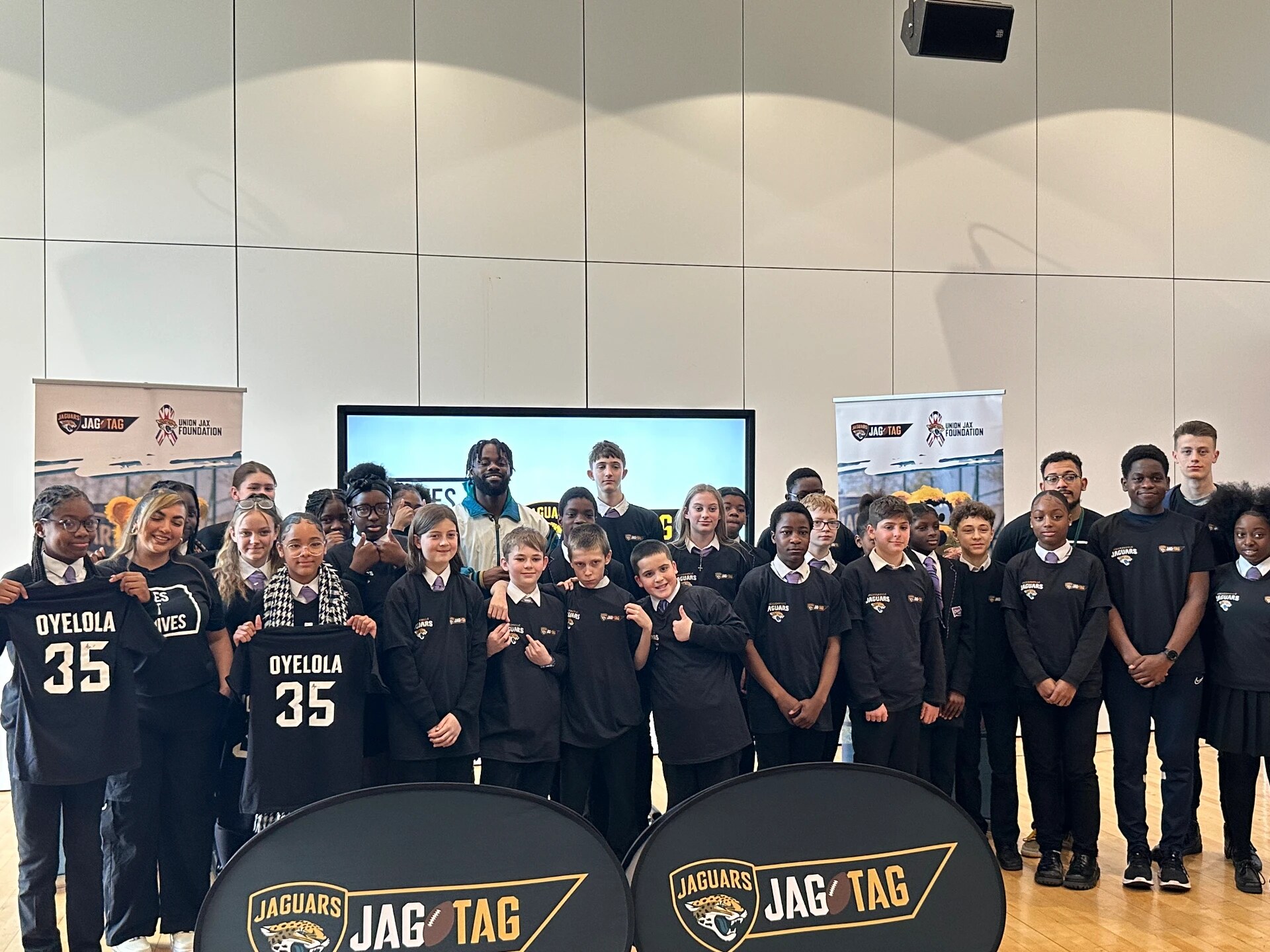 Ayo Oyelola with a large group of school pupils holding Oyelola jerseys at a Jag Tag event