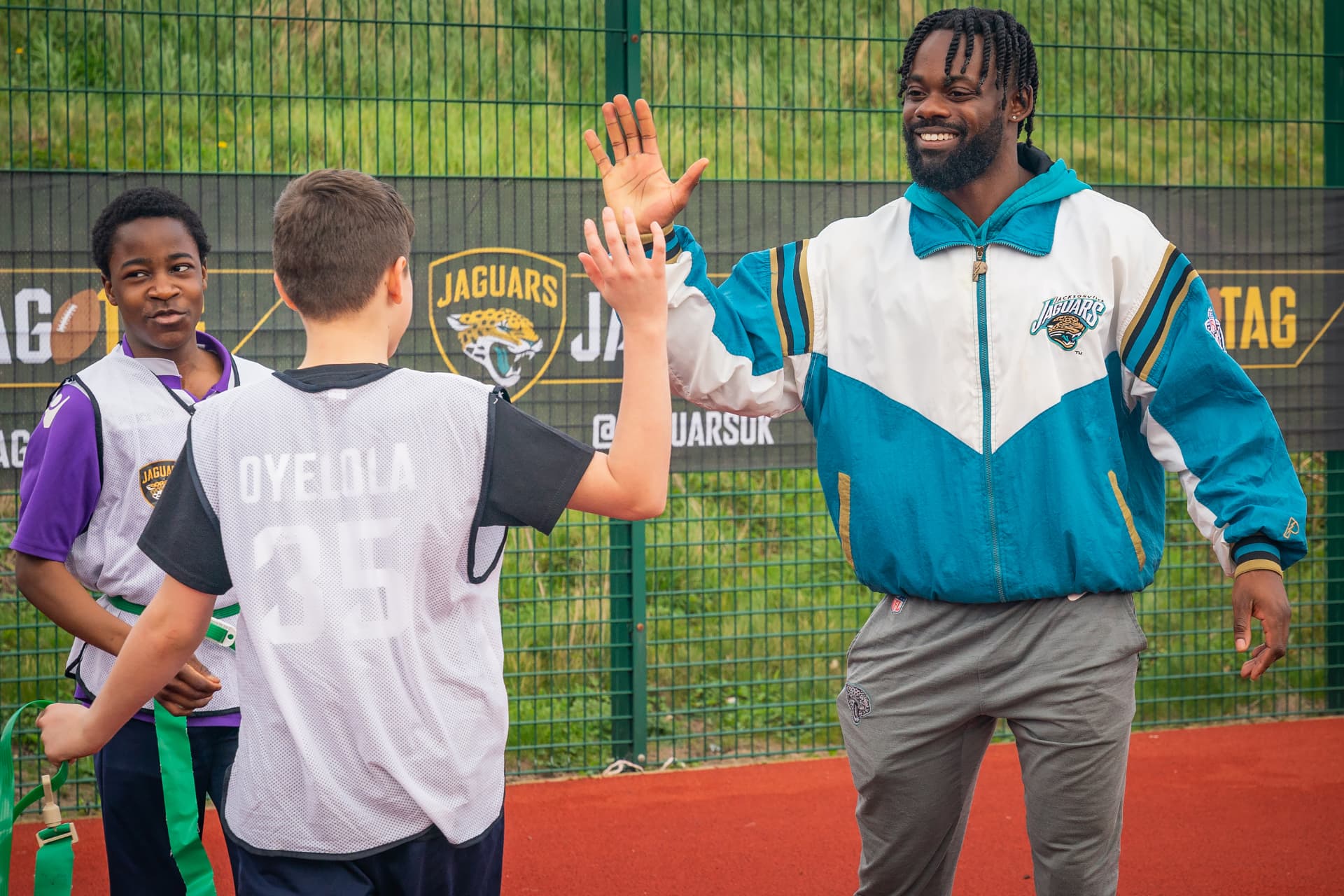 Ayo Oyelola high-fiving a young player wearing an Oyelola jersey at a flag football session